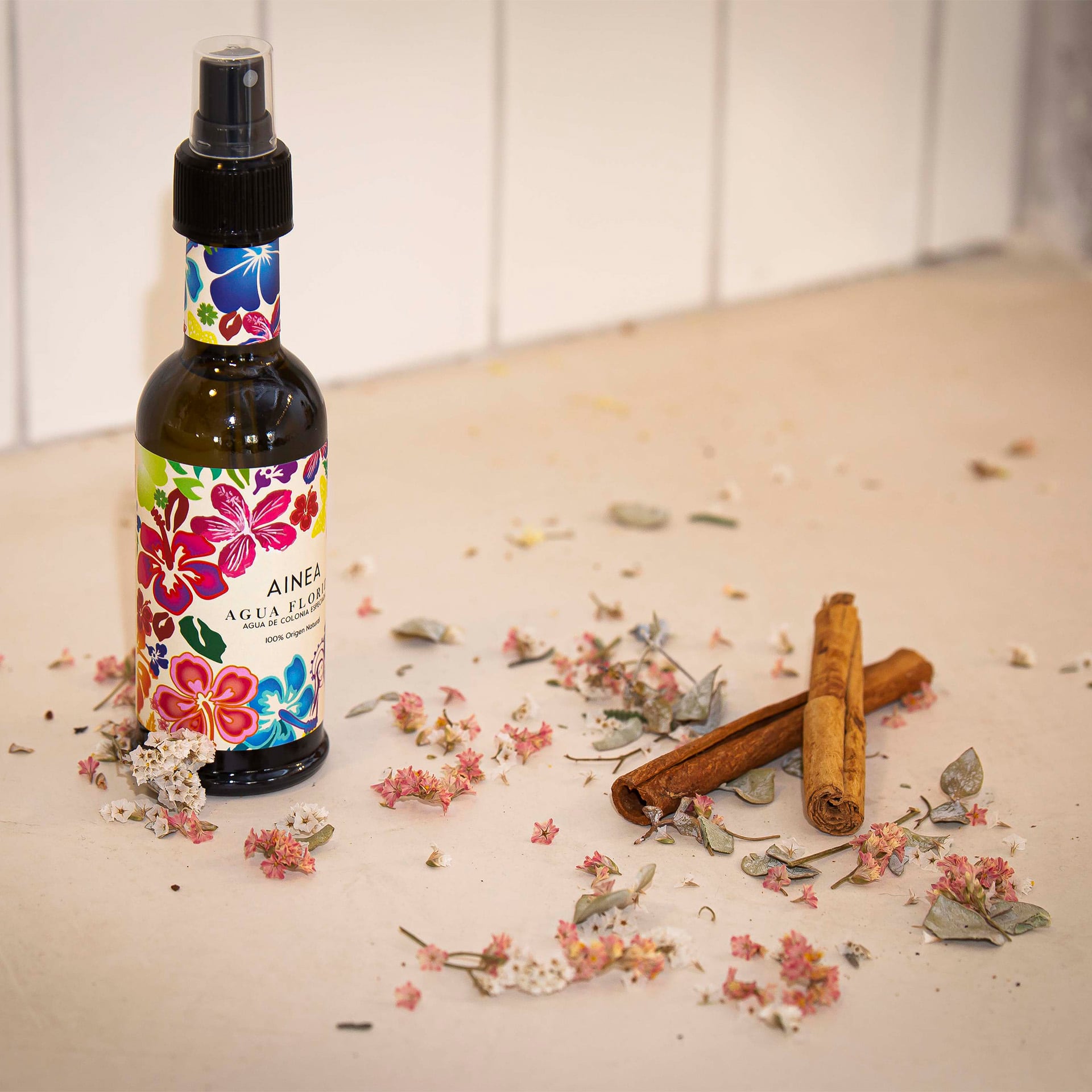 Imagen hecha desde arriba del Agua Florida 100 ml de Ainea Perfums con flores y ramas de canela como atrezzo.