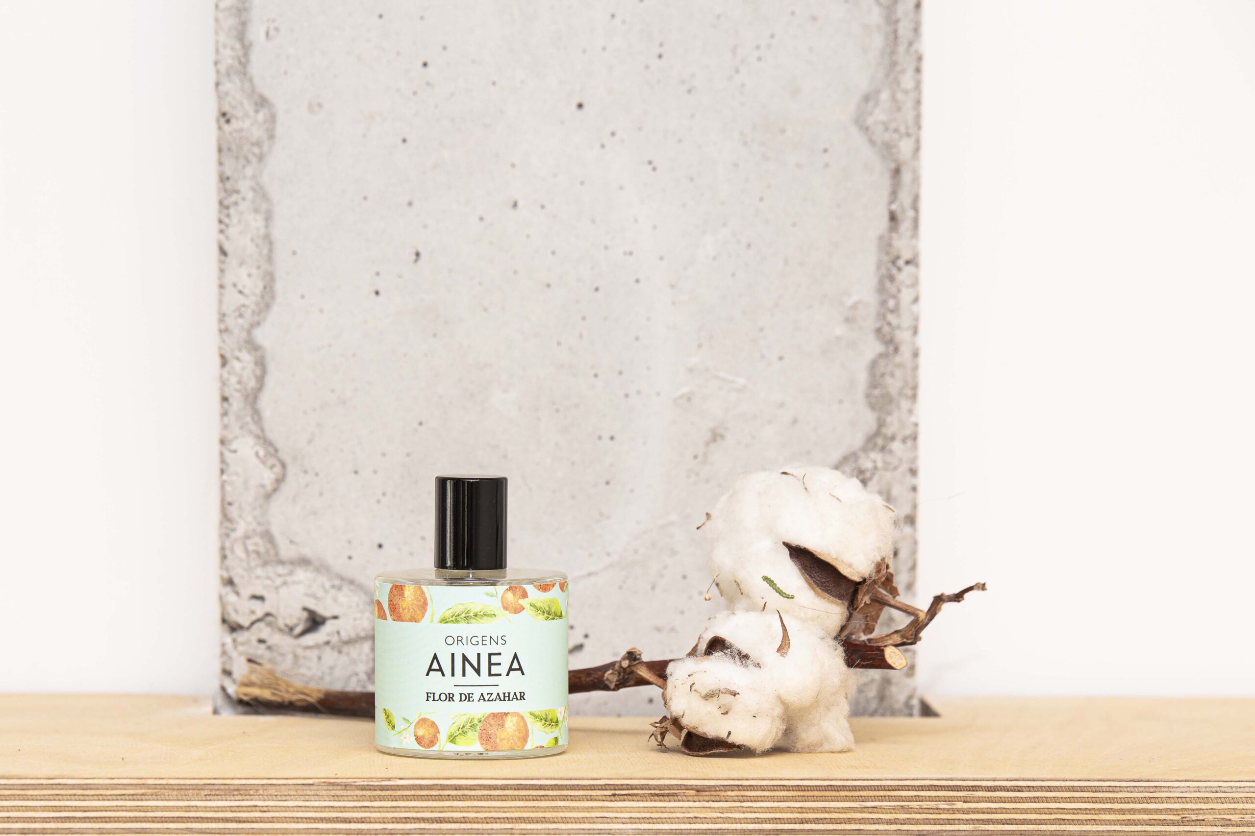 Colonia Flor de Azahar 50 ml de la colección Origens de Ainea Perfums con rama de algodón y pared de cemento de fondo.
